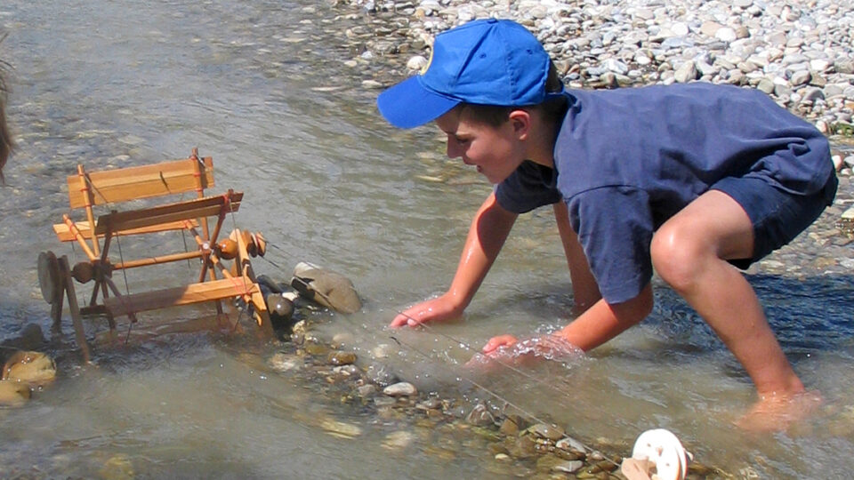 Ein Kind spielt mit Wasserrad von Kraul Holzspielwaren am Fluss